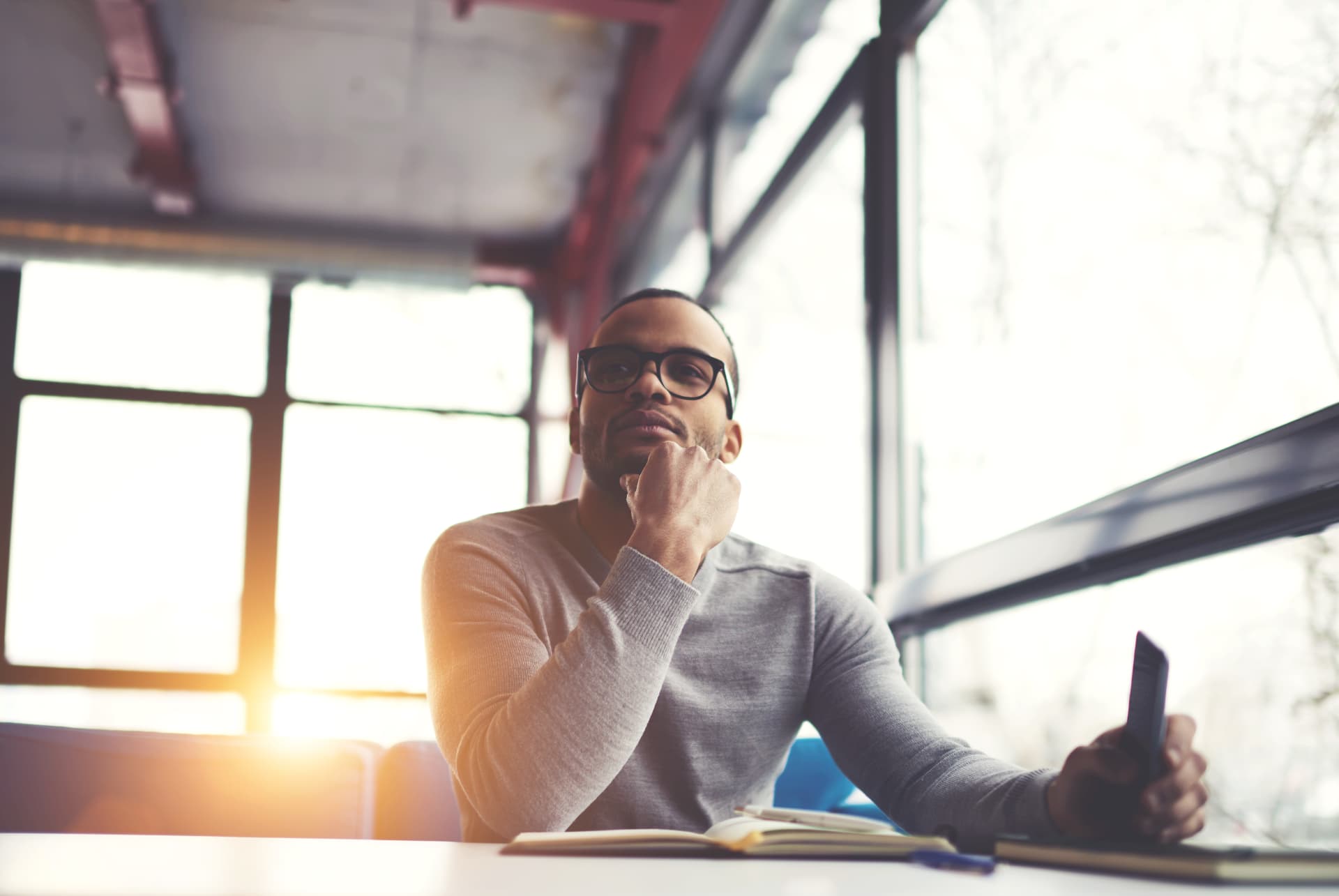 Man in glasses thinking at his laptop by a sunlit window